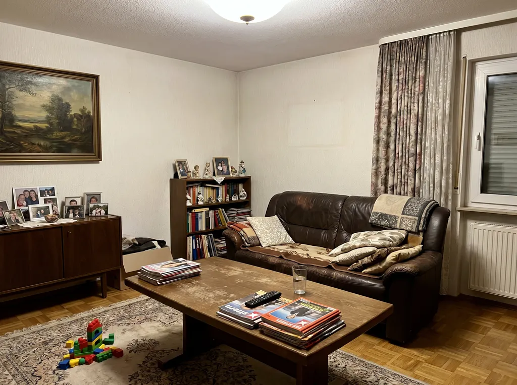 Wohnzimmer mit persönlicher Einrichtung des Eigentümers: dunkles Ledersofa, Familienfotos, Kinderspielzeug auf dem Boden